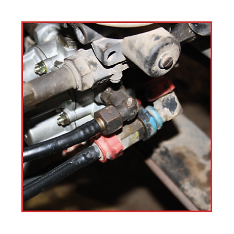 Nahaufnahme eines Motorradteils: Rohre, Schrauben, und rote/blaue Abdeckungen.